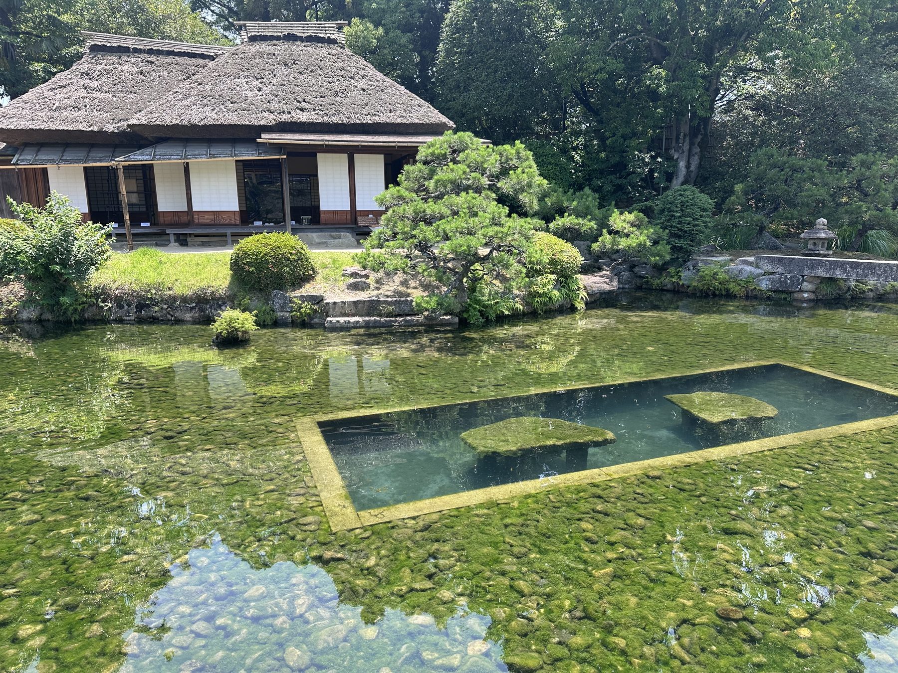 A thatched roof house reflected in a still garden pond
